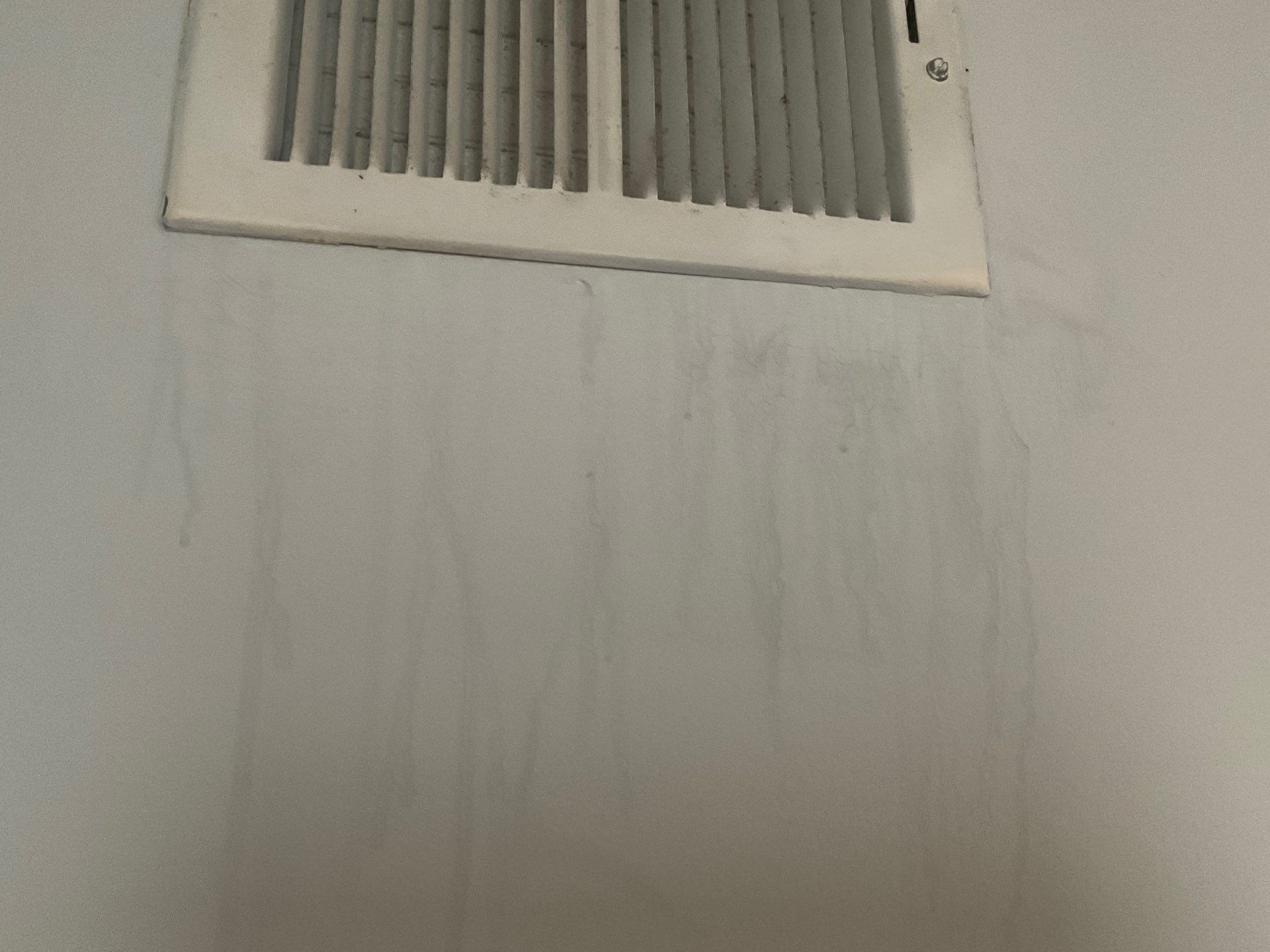 Water damage on ceiling below air conditioning vent, showing streaking and discoloration.